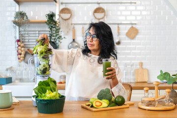 Portrait senior healthy asian woman making green vegetables detox cleanse and green fruit smoothie with blender.elderly woman drinking glass of green fruit smoothie in kitchen.healthcare, insurance. - Powered by Adobe
