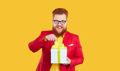 Funny happy excited bearded fat man opens gift box isolated on vivid yellow background. Young...