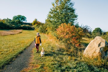 A boy walks with a corgi dog in the autumn forest