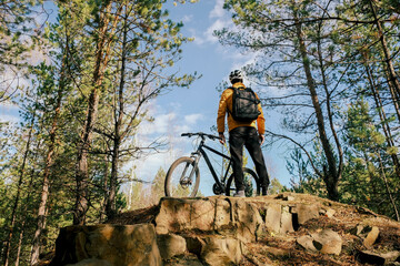 active lifestyle.A cyclist in equipment with a backpack stands with his back with a bicycle on a mountain against the sky.Mountain Bike
