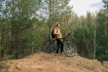 Fototapeta premium active lifestyle.A cyclist in equipment with a backpack is leaning on a bicycle on a mountain and looking at the landscape.Mountain Bike