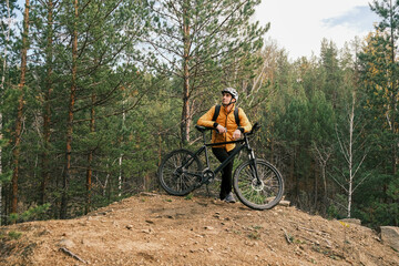 Fototapeta premium active lifestyle.A cyclist in equipment with a backpack is leaning on a bicycle on a mountain and looking at the landscape.Mountain Bike