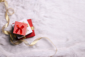 Stack of various presents gift boxes with gold ribbon on white fur background, top view. Boxing day sale seasonal promotion background.