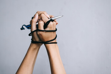 Hands with silver pen tied with rope, depicting the idea of freedom of the press or freedom of expression and international human rights day concept. - obrazy, fototapety, plakaty