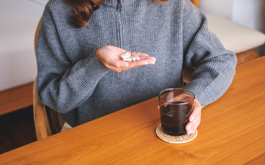 Closeup image of a woman holding pills and a glass of water