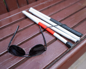 Sunglasses and a folding cane for the blind on a bench. 