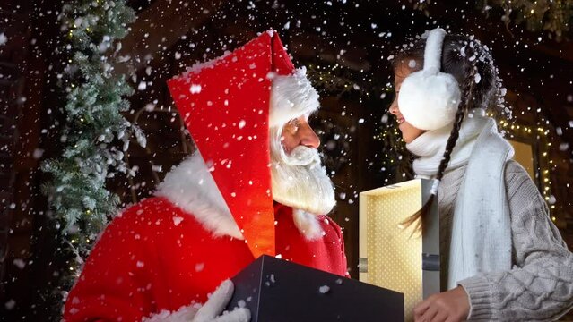 Festive tradition of Santa Claus giving magical gift box child girl under snow fall on Christmas night. Holiday spirit, wished surprise present and kid dream