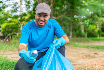 Volunteering, charity and clean environment concept. Happy asian man of volunteers with garbage bags wearing blue t-shirt and cleaning area in park or roadside, copy space.