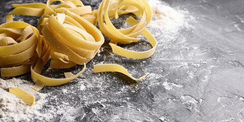 Homemade uncooked pasta fettuccine with flour over dark background