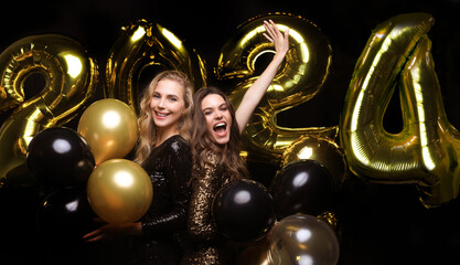Happy gorgeous girls in stylish sexy party dresses holding gold 2024 balloons, having fun at New Year's Eve Party.