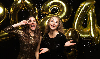 Happy gorgeous girls in stylish sexy party dresses holding gold 2024 balloons, having fun at New...