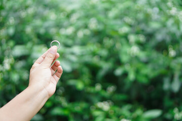 Close up hand hold silver ring, outdoor background. Concept, accessory, jewelry. Ring is the symbol or classic representation of love, engagement and wedding.              