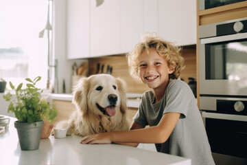 Cheerful little boy is posing with a golden retriever dog at the kitchen table. Funny kid and his pet preparing for breakfast at home. Happy smiling boy and puppy enjoy their time spent together.