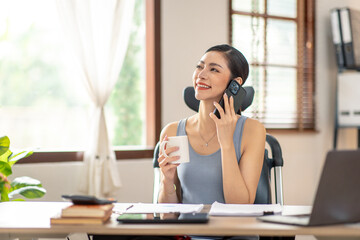 Obraz premium Asian Woman entrepreneur busy with her work in the office. Young freelancer Asian woman talking over smartphone or cellphone while working on computer at her desk.