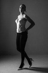 Beauty, fashion, style and make-up concept. Beautiful woman full body silhouette portrait. Part of model covered in shadow. Model wearing white corset and high heels. Black and white image