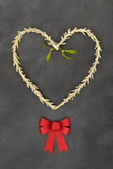 Christmas gold tinsel heart shape wreath, red bow,  mistletoe sprig. Traditional romantic symbols for the festive holiday season on grunge gray background.