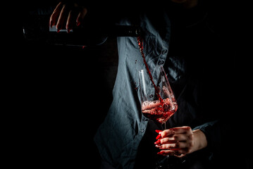 woman hands pouring red wine into a glass from a bottle on black background