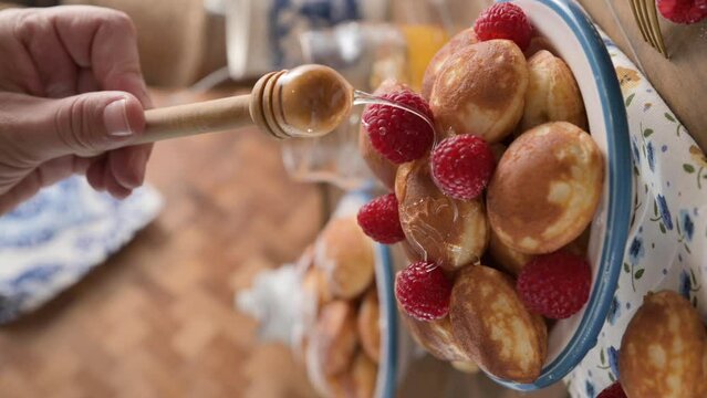  Close-up of golden Dutch Poffertjes with syrup and berries. Delicious traditional mini pancakes on a plate. the , honey pours on mini pancakes in a white plate with a blue pattern