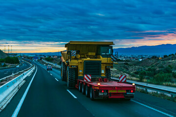Gondola truck for special transport transporting a dumper truck on the highway at sunrise. - obrazy, fototapety, plakaty