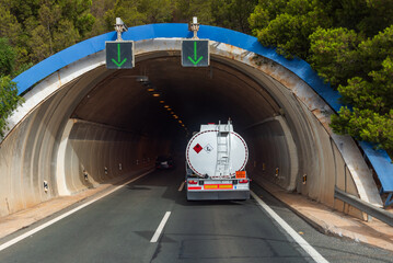 Rear view of a fuel tanker truck, dangerous goods, entering a tunnel on a highway. - obrazy, fototapety, plakaty