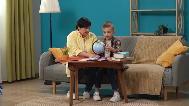 Close up shot of senior woman and little kid in the room sitting on the couch, boy holding a small globe and looking at the map.
