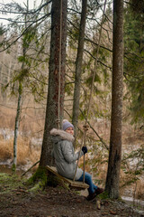 woman sitting on swings in the middle of the forest in cold winter time, warm clothes 