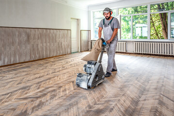 Professional carpenter worker grinding a wooden parquet floor by using floor sander - obrazy, fototapety, plakaty
