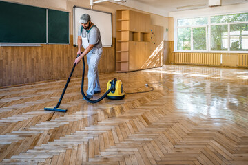 Worker carpenter cleans the parquet floor with professional vacuum cleaner. Industrial theme - obrazy, fototapety, plakaty
