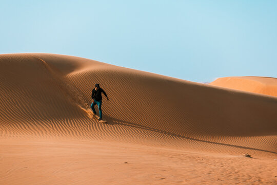 High quality stock photo of a man sliding down with a sand board in a dune in the Sultanate of Oman. - Powered by Adobe