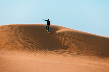Man sliding down with a sand board in a dune in the Sultanate of Oman.
