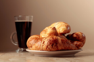 Freshly baked croissants and black coffee on a beige ceramic table.