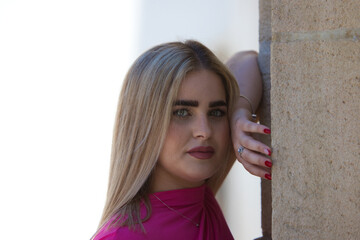Young and beautiful blonde woman with overweight is leaning on the wall and dressed in casual and modern clothes. The woman stares at the camera with an expressionless face.
