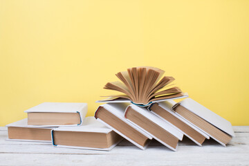 Open books, hardback colorful books on wooden table. yellow background. Back to school. Copy space for text. Education business concept.