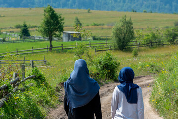 Two muslim girls walking on the rural mountain road with beautiful landscape in front of them. Women with hijab in nature representing islam religion