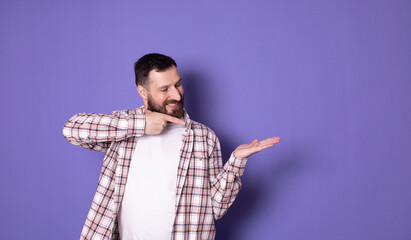 Positive young bearded man  holding something invisible in his hands and smiling at camera, posing...