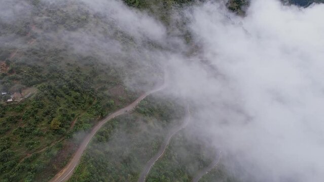 A cinematic drone view of misty or foggy clouds.mountain peaks and a curvy road