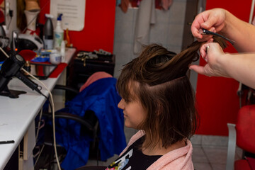 Professional female hairdresser cutting girl's brown hair in salon, closeup