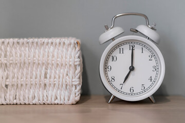 Close-up of a round white alarm clock on a table in the bedroom. The hands on the clock show seven...