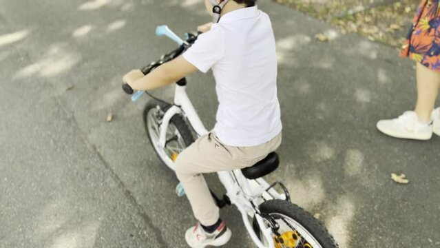 Helmeted Young Boy Demonstrates Riding Without Training Wheels and Pedals His Equipped and Secure Bike Ahead of His Parents on a Tree-Lined Sidewalk