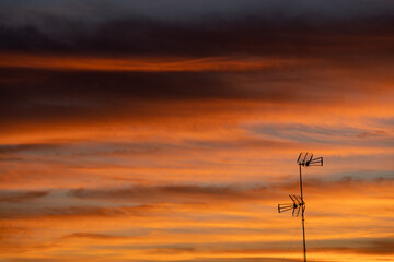 Fototapeta na wymiar a sunset cloudscape image filled with golden clouds and a single television antenna silhouette.