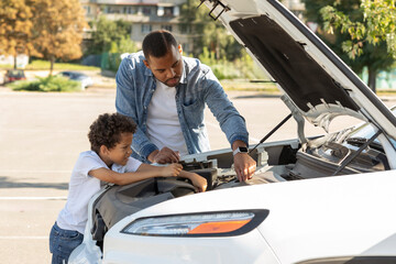 Black father and preteen son checking car engine outdoors - Powered by Adobe