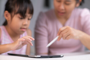 Happy little Asian daughter talking with mother using digital tablet to do homework or study...