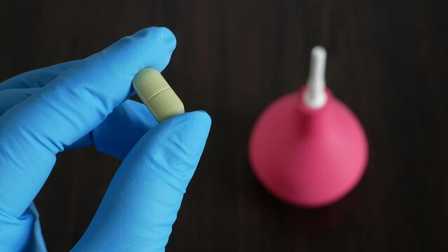 hand holding  pills on enema  on wooden background, enema vs pills for treatment  from intestinal constipation