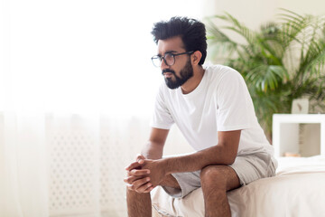 Young Pensive Eastern Man Sitting In Bed And Looking Away,