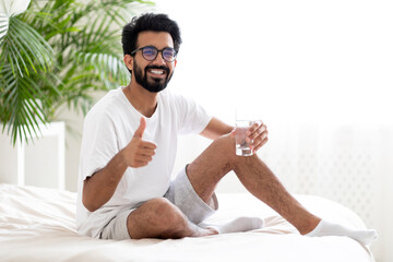 Smiling Young Indian Man Holding Glass With Water And Showing Thumb Up