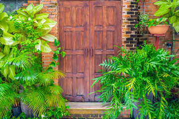 wooden door with a brick wall and green plants decorating it.
