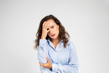 Young stressed woman at work, pressing hand to forehead, evident headache and work stress