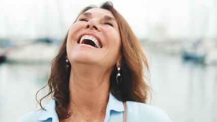 Close up, happy attractive middle age woman standing in port on yacht background looking at camera...
