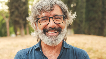 Close-up of retired man with glasses crossing his arms and looking at the camera with smile while...