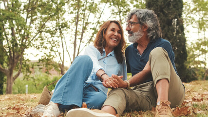 Beautiful retired couple spending time together outside, sitting on the grass in the park in autumn